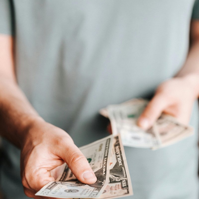 Close-up of an unrecognizable man holding dollar bills with a blurred background indoors.