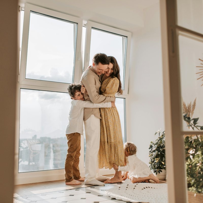 A happy family embracing near a large window in a bright, cozy room filled with natural light.