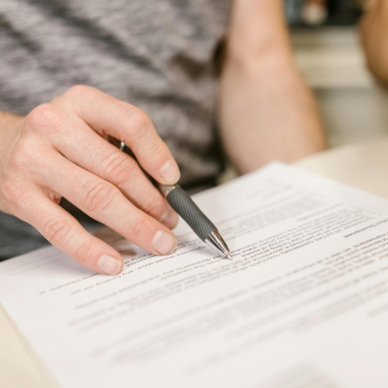 Close-up of a person's hand signing an important legal document with a pen indoors.
